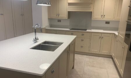 Re-sprayed modern kitchen with refreshed beige cabinetry, a central island featuring a double sink and chrome fixtures, illuminated by pendant lights.