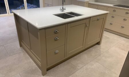 Re-sprayed modern kitchen with refreshed beige cabinetry, a central island featuring a double sink and chrome fixtures, illuminated by pendant lights.