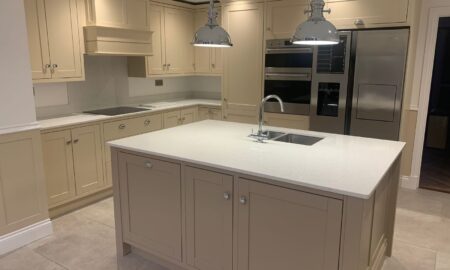 Re-sprayed modern kitchen with refreshed beige cabinetry, a central island featuring a double sink and chrome fixtures, illuminated by pendant lights.
