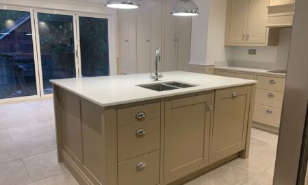 Re-sprayed modern kitchen with refreshed beige cabinetry, a central island featuring a double sink and chrome fixtures, illuminated by pendant lights.